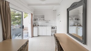 A modern kitchen with white cabinets, a microwave, and a sink. There is a large mirror on the wall and a sliding glass door leading to an outdoor area. - Manly Oceanside (Sydney)