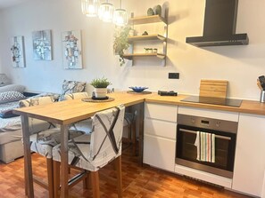 A modern kitchen with a wooden table, built-in oven, and pendant lights.