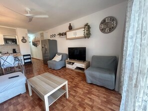 A modern living room with a flat-screen TV, a sofa, a coffee table, and a kitchen area in the background.
