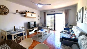 A living room with a TV, dining table, chairs, sofa, and a ceiling fan. - Mareverde spacious 1 bedroom apartment (Costa Adeje)