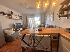 A modern living room with a wooden dining table, grey sofa, and a TV on a stand.