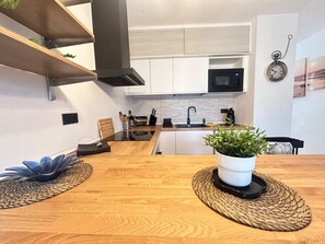 Eine moderne Küche mit weißen Schränken, einer schwarzen Mikrowelle und einem Holztisch mit einem Blumentopf.