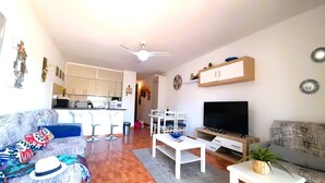 A living room with a sofa, a coffee table, a TV, and a kitchen in the background. - Mareverde spacious 1 bedroom apartment (Costa Adeje)