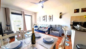 A dining area with a table set for two, a bottle of wine, and two glasses. There is a sofa and a television in the background. - Mareverde spacious 1 bedroom apartment (Costa Adeje)