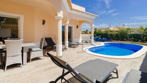 A poolside area with lounge chairs, a table, and a covered patio. - Poolvilla Casa Vista Mar (Carvoeiro)