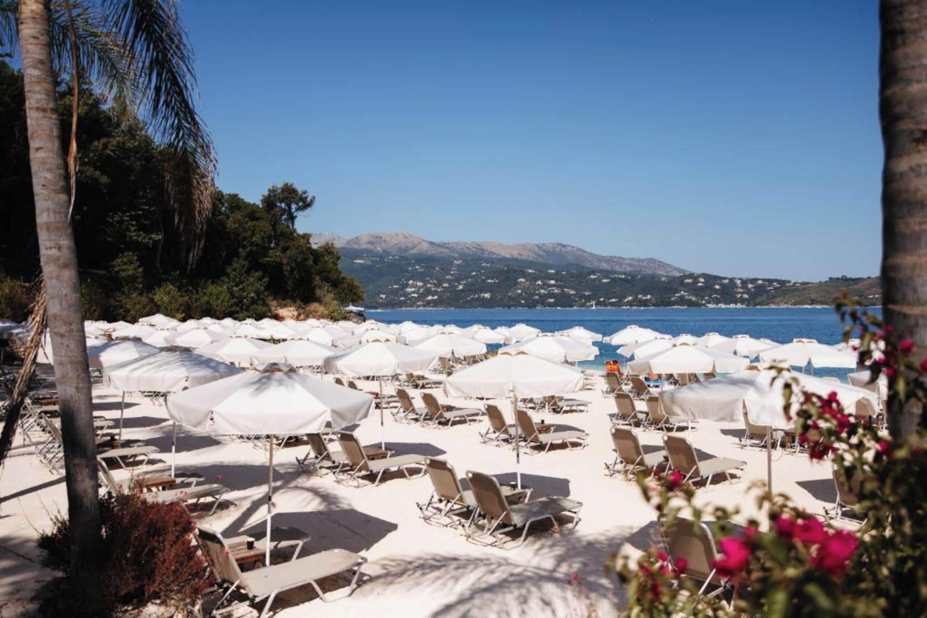 A beach with rows of sun loungers and umbrellas, a clear blue sky, and a mountain in the background.