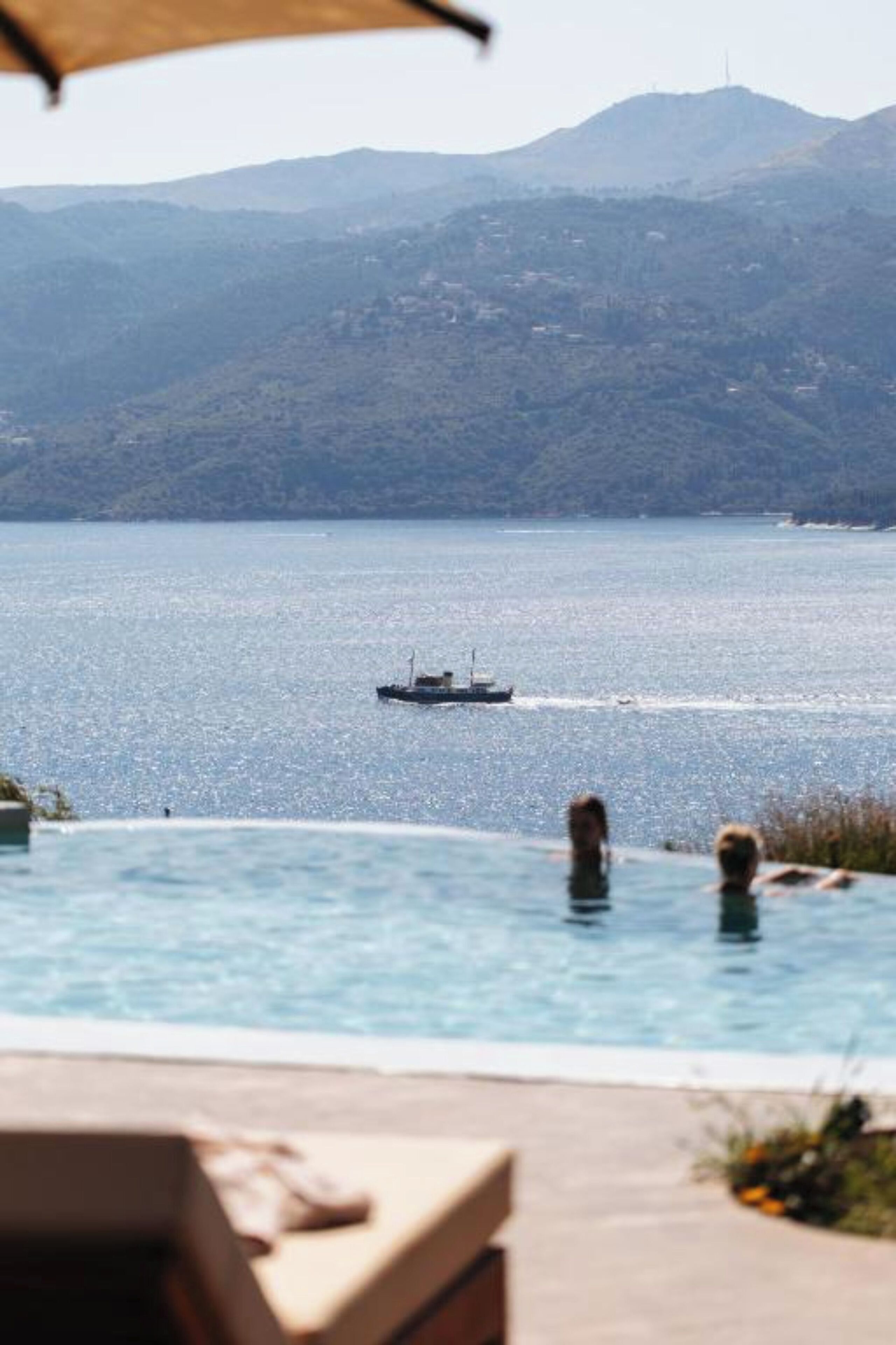 Une piscine offrant une vue sur un bateau sur l’eau et sur des montagnes en arrière-plan.