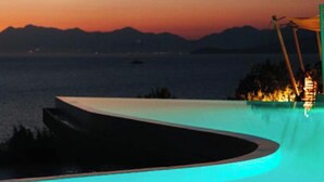 A pool with a curved edge and a view of the sea and mountains at dusk. - Arameras Resort (Ksamil)
