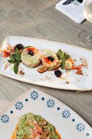 A plate of seafood appetizer with shrimp, avocado, and garnishes on a white plate.