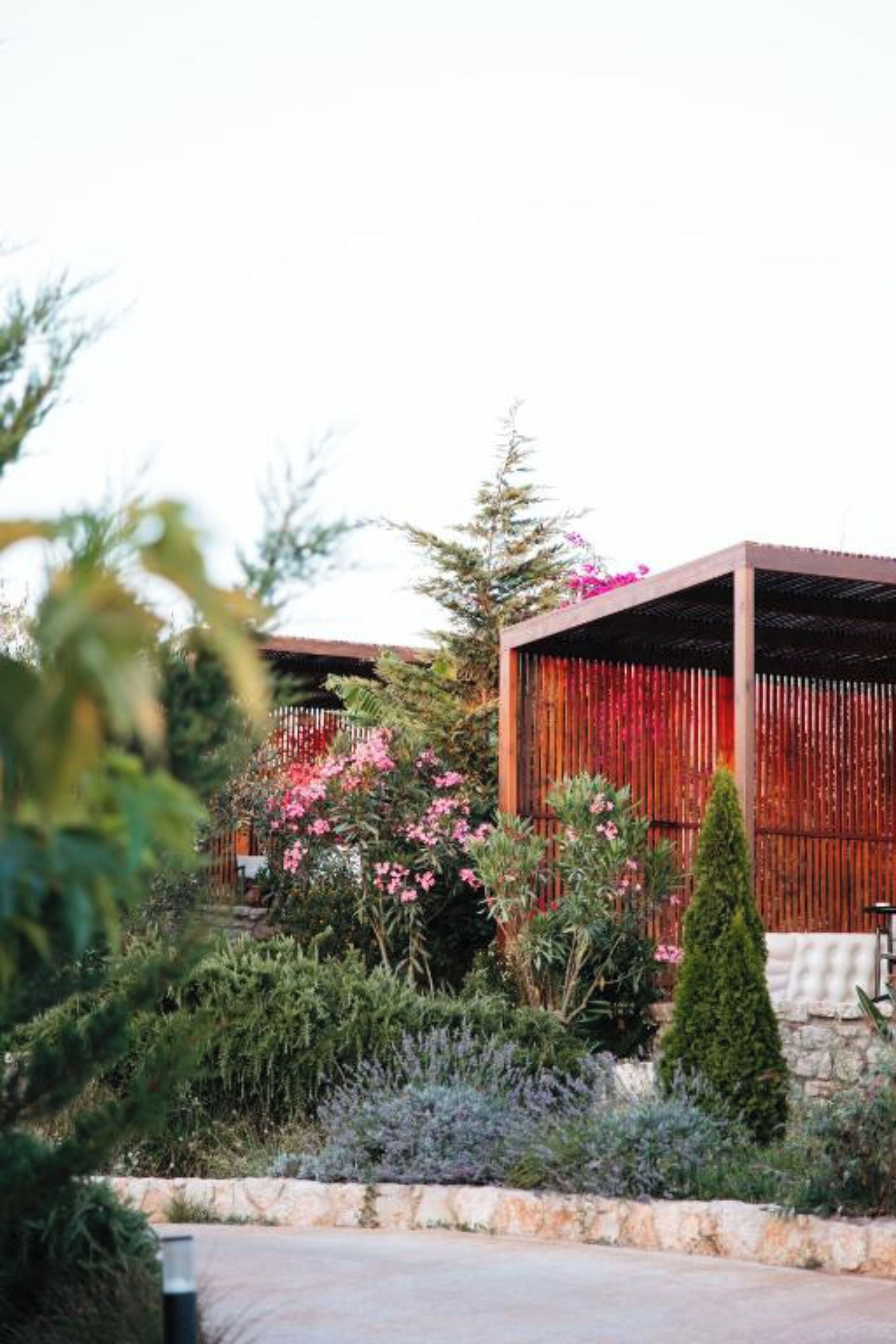 Un bâtiment moderne doté d’une façade en bois et d’un socle en pierre, entouré d’une végétation luxuriante et de plantes en fleurs.