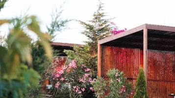Un bâtiment moderne doté d’une façade en bois et d’un socle en pierre, entouré d’une végétation luxuriante et de plantes en fleurs.