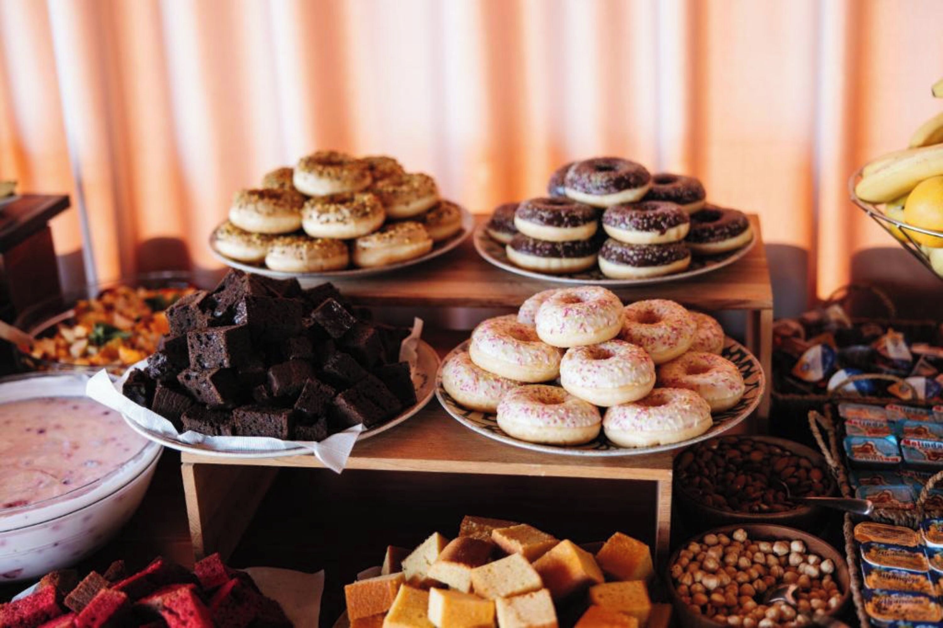 Uma mesa de buffet com diversos doces, incluindo donuts, brownies e outras sobremesas.