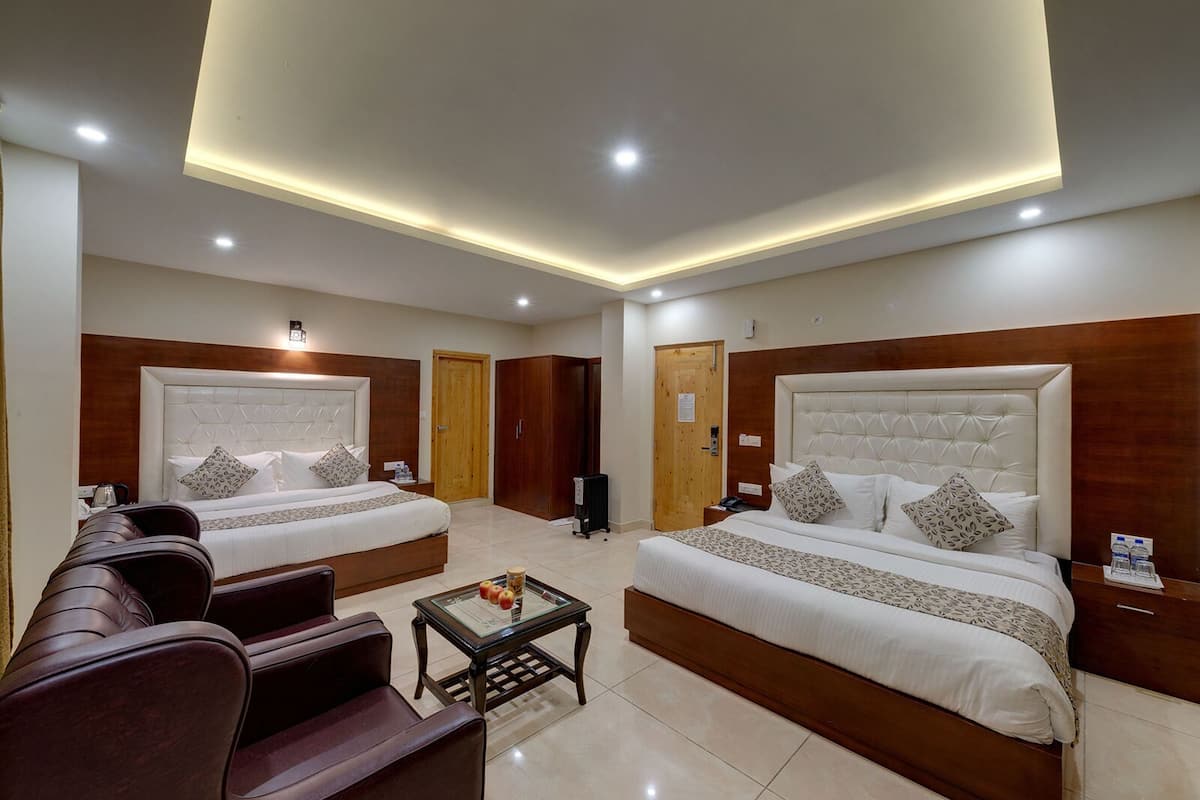 A hotel room with two beds, a sofa, a coffee table, and a wooden wardrobe.