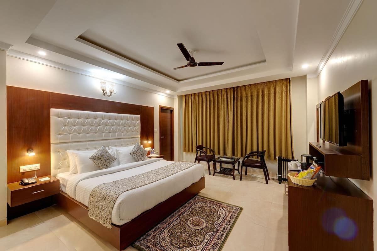 A hotel room with a large bed, a desk, two chairs, a television, and a ceiling fan.