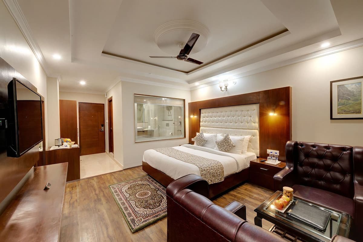 A hotel room with a bed, a leather sofa, a TV, a desk, and a large mirror.