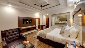 A modern hotel room with a large bed, a leather armchair, a TV, a mirror, and a ceiling fan. - Regenta Place Green Leaf Manali- A Centrally Heated Resort (Manali)