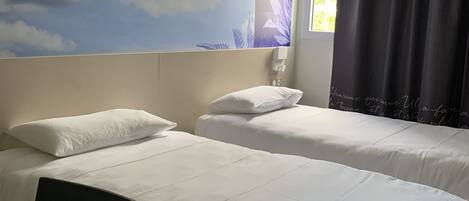 A hotel room with two beds, a desk, and a large wall mural of clouds.