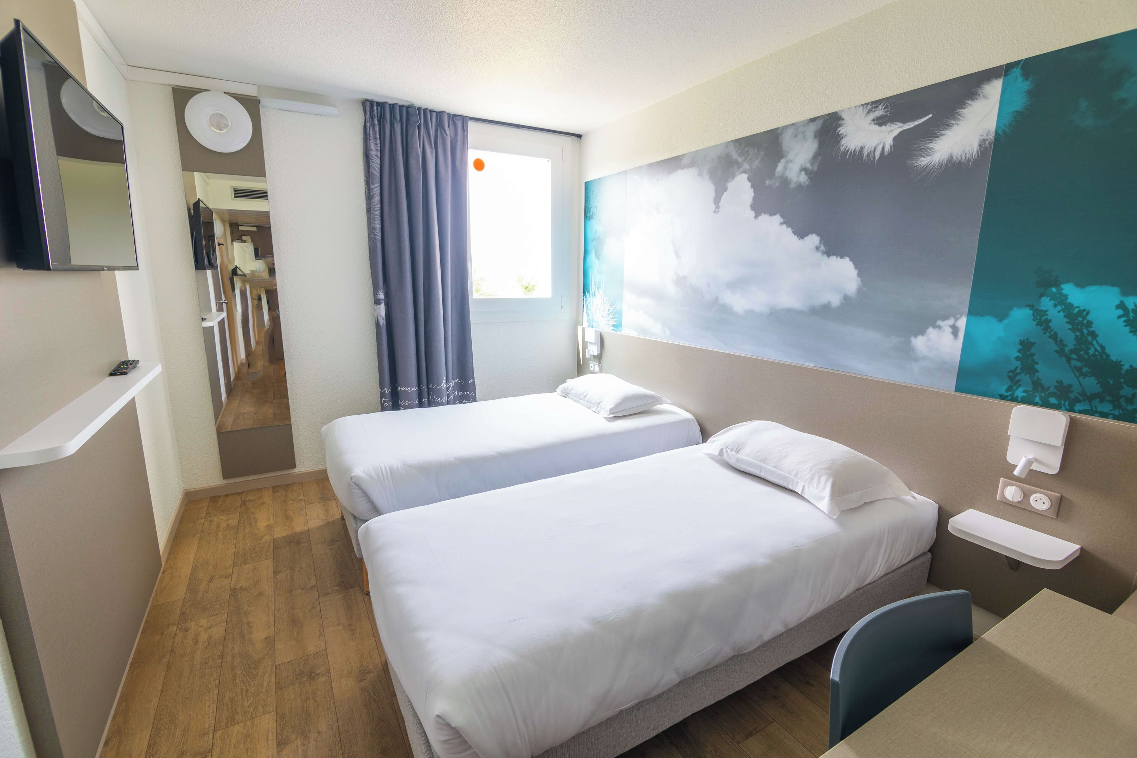 Habitación de hotel con dos camas, un escritorio, una silla, un televisor y una ventana con cortinas.