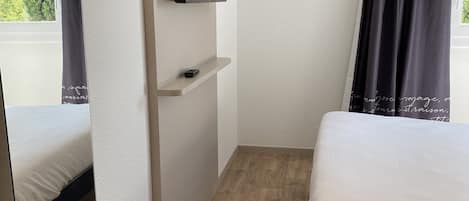Un dormitorio con una cama, un televisor instalado en la pared, un estante y una ventana con cortinas.