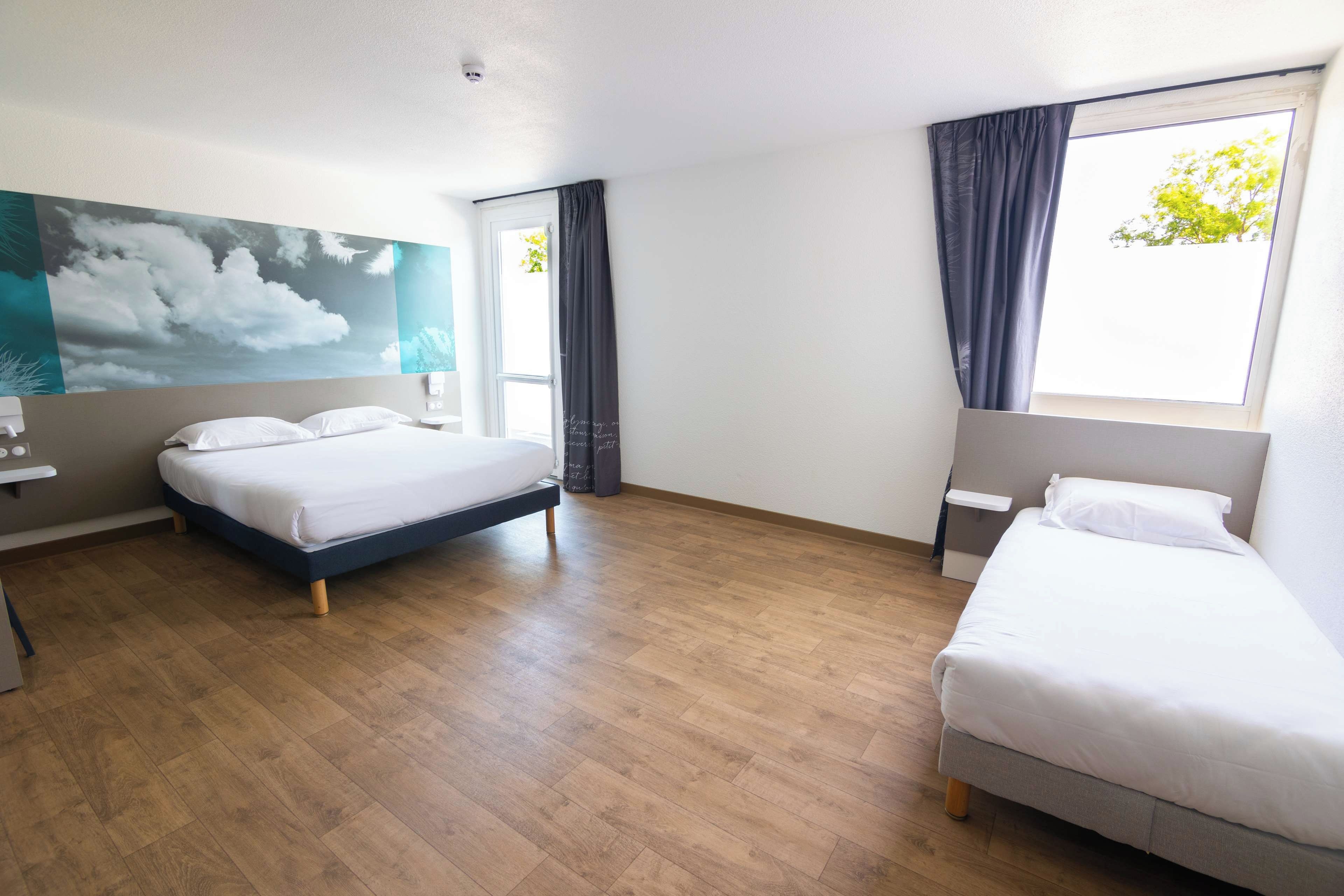 Una habitación de hotel con dos camas, un cuadro grande y un ventanal con cortinas.