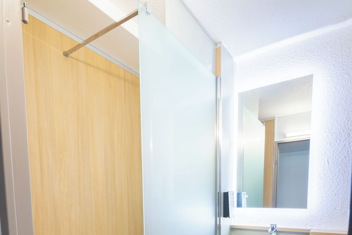 A bathroom with a glass shower enclosure, a white sink, and a wooden floor.