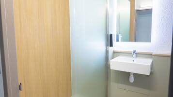 Un bagno con box doccia in vetro, lavandino bianco e pavimento in legno.