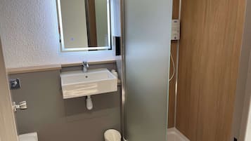 Un baño con un lavamanos blanco, un espejo, un inodoro y una puerta de madera.