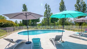 A swimming pool area with lounge chairs and umbrellas, surrounded by a fence and trees. - Kyriad Direct  - Bourg les Valence (Bourg-les-Valence)