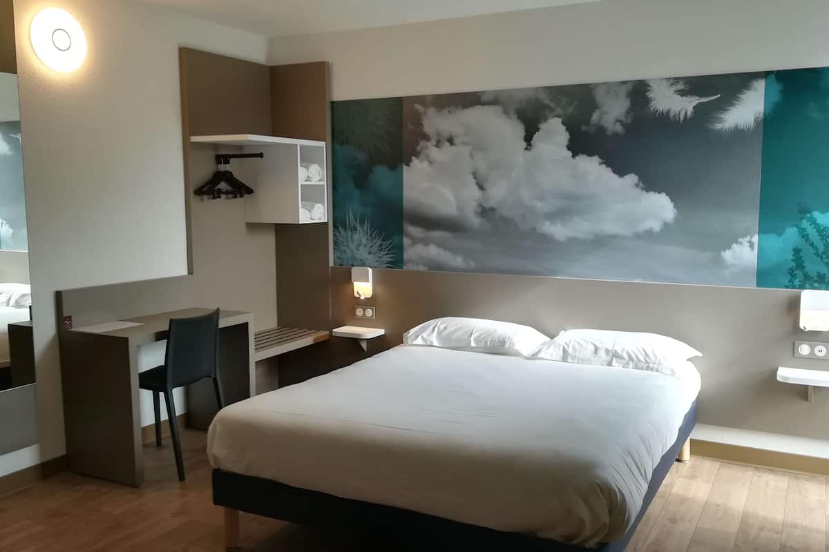 A hotel room with a bed, a desk, a chair, a mirror, a wardrobe, and a large wall mural.