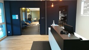 A reception area with a desk, chairs, and a seating area with tables and chairs. - Kyriad Direct  - Bourg les Valence (Bourg-les-Valence)
