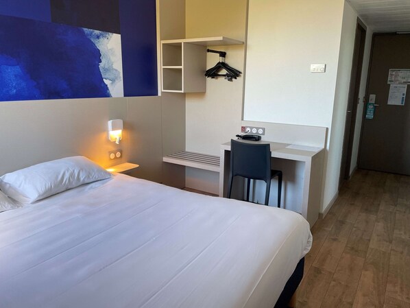 Ein Hotelzimmer mit Bett, Schreibtisch, Stuhl, Wandregal und Wandlampe.