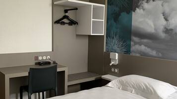 Une chambre d’hôtel équipée d’un lit, d’un bureau, d’une chaise et d’une étagère fixée au mur, avec un cintre noir.