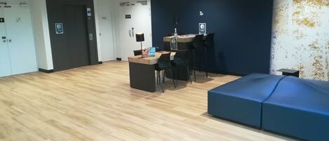 A spacious room with a wooden floor, a reception desk, a blue sofa, and a wall with a Wi-Fi symbol.