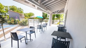An outdoor patio with tables and chairs, a pool, and a covered area with a view of the pool. - Kyriad Direct  - Bourg les Valence (Bourg-les-Valence)