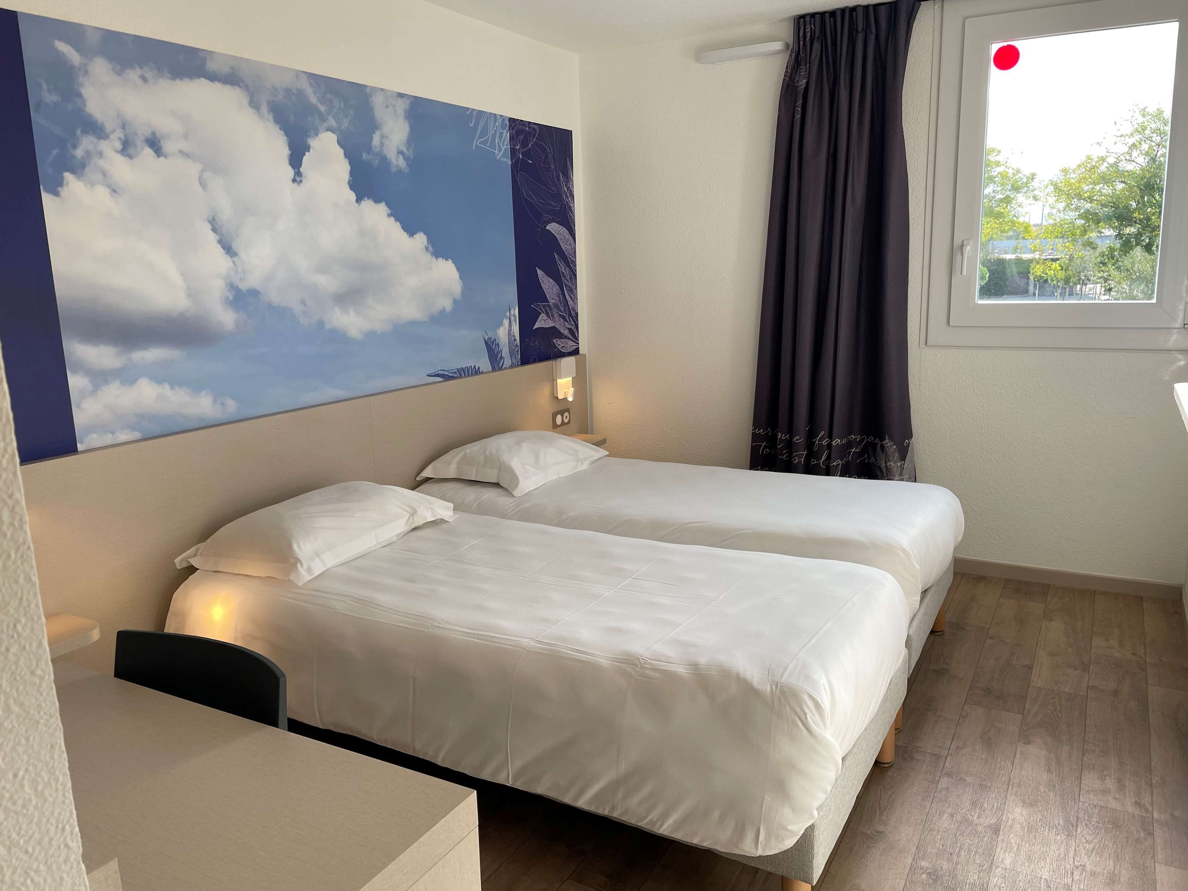 Habitación de hotel con dos camas, un escritorio, un mural grande en la pared y una ventana con cortinas.
