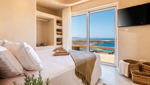 A bedroom with a large bed, a TV, and a balcony with a view of the sea. - Breathtaking 5 Bedroom Villa With Private Pool (Mykonos)