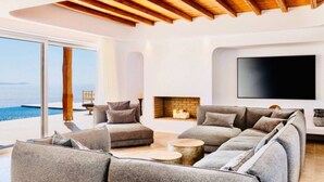 A modern living room with a large sectional sofa, a flat-screen TV, and a fireplace. - Breathtaking 5 Bedroom Villa With Private Pool (Mykonos)