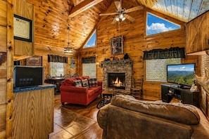 A log cabin interior with a fireplace, a red sofa, a television, and a stone fireplace surround.