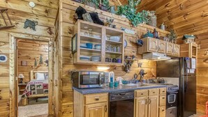 A wooden cabin interior with a kitchen area featuring a microwave, stove, refrigerator, and wooden cabinets. - Another Day In Bearadise- “Cozy Cabin Retreat in the Smokies – Comfort & Fun!!! (Pigeon Forge)