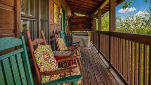 A wooden porch with green chairs and a bench, a wooden ceiling, and a view of trees. - Another Day In Bearadise- “Cozy Cabin Retreat in the Smokies – Comfort & Fun!!! (Pigeon Forge)
