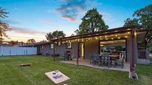 A covered patio area with a table and chairs, a barbecue grill, and string lights. - 5BR House by Lambeau with Game Garage (Green Bay)