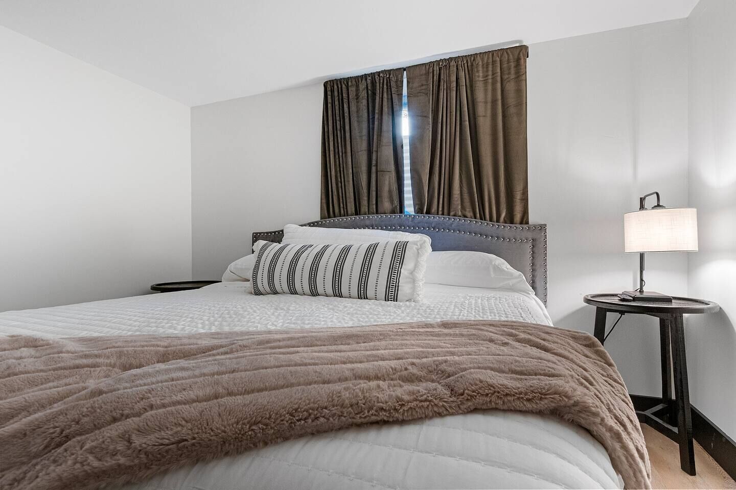 A neatly made bed with a fluffy brown blanket, a headboard, and a bedside lamp.