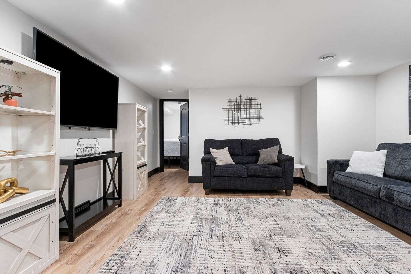 Un salon moderne avec un canapé gris, un téléviseur noir et un tapis à motifs.