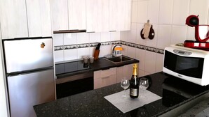A kitchen with white cabinets, a black countertop, a microwave, a sink, and a bottle of champagne. - Mareverde Sun apartment, pool view (Costa Adeje)