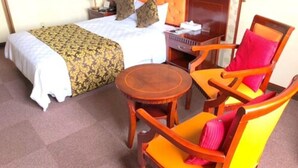 A hotel room with a bed, a nightstand, a wooden chair with cushions, and a small round table. - Hotel Robinson INN Ryukyu Tabikan MW1 (Okinawa)