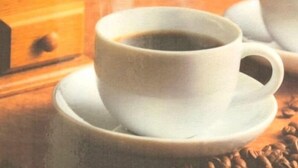 A cup of coffee on a saucer with a wooden surface and a drawer in the background. - Hotel Robinson INN Ryukyu Tabikan MW1 (Okinawa)