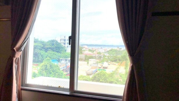 A window with curtains, offering a view of a residential area with buildings and greenery. - Hotel Robinson INN Ryukyu Tabikan MW1 (Okinawa)