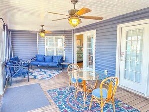 A covered porch with a table and chairs, a blue sofa, and a ceiling fan. - Casa de Verde (North Myrtle Beach)
