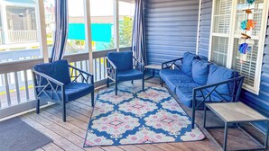 Een overdekt terras met blauw meubilair, een gekleurd vloerkleed en een plafondventilator.