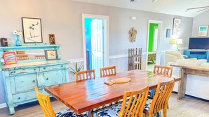 Een eethoek met een houten tafel en stoelen, een blauwe dressoir met decoratieve objecten, en een groene deur op de achtergrond.